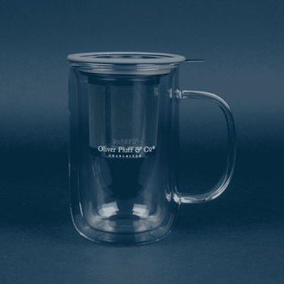 clear glass mug that reads 'oliver pluff & co' with stainless steel brewing basket resting inside and grey lid on blue background