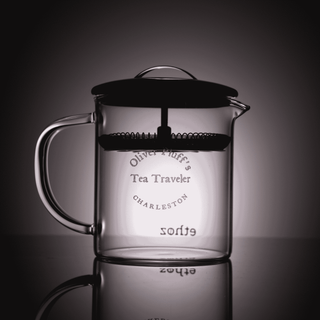 Clear glass tea press with black lid on a reflective surface