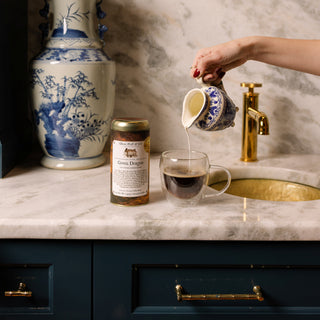 green dragon coffee tin on msrble countertop next to clear coffee cup being filled with milk