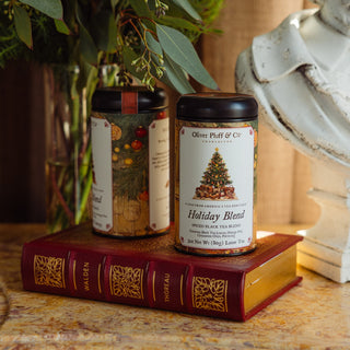 two holiday blend tea tins sitting on top of a red book on a marble tabletop