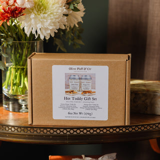 hot toddy gift set in brown kraft box on wooden tabletop with flower arrangement in the background
