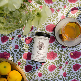 Jasmine tea packaging on a floral tablecloth with a cup of tea and lemons.