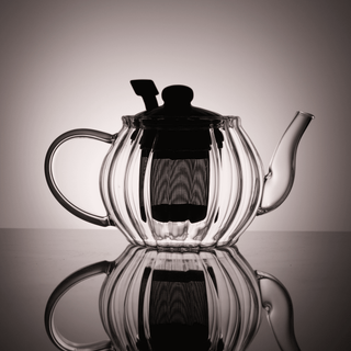 Clear glass teapot backlit to show interior strainer on a reflective surface