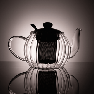 Clear glass teapot backlit to show interior filter and lid on a reflective surface