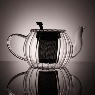 Clear glass teapot backlit to show interior filter on a reflective surface