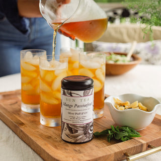 Sun Tea tin with glasses of iced tea on a wooden tray outdoors.