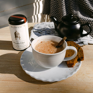 Cup of masala chai with a tin of masala chai mix on a wooden table.