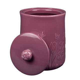 Purple ceramic jar with floral embossing and matching lid on a green background