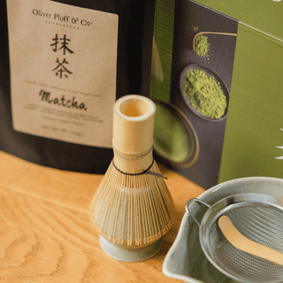 Bamboo matcha whisk and ceramic whisk holder beside an Oliver Pluff Matcha Gift Set, matcha bowl, scoop, and sifter