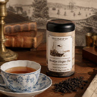 Tea canister labeled 'Oliver Pluff & Co' with a cup of tea and loose tea leaves on a wooden surface.