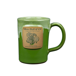 green mug with white glazing on top that reads oliver pluff with tea blossom design