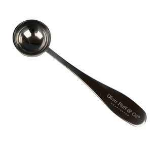 A stainless steel measuring spoon with a long handle, featuring the engraved brand name 'Oliver Platt & Co' and 'CREATION' on the handle, set against a solid dark green background.