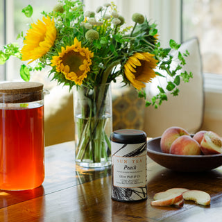 Sun tea with peach flavor, sunflowers, and peaches on a wooden table.