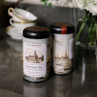 Two tea canisters with decorative labels on a reflective surface.