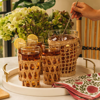 three glasses and a pitcher containing iced tea sitting on a table top with woman stirring the pitcher