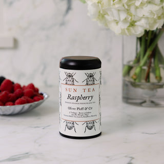 Sun Tea Raspberry canister on a marble surface with raspberries and flowers in the background
