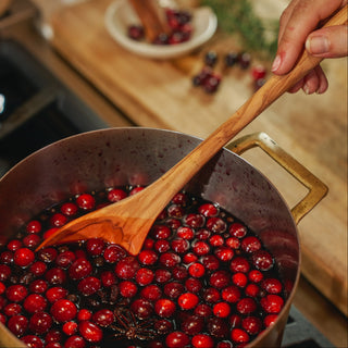 Cranberries being cooked in a pot with a wooden spoon