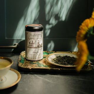 Tea canister labeled 'Single' on a decorative tray with tea leaves, sunflower, and teacup.