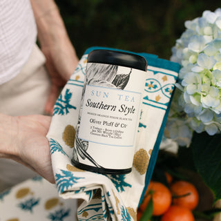 hands holding a southern style tea tin in a napkin in an outdoor setting
