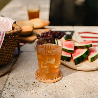 Glass of iced summer toddy on a stone surface with watermelon slices and grapes in the background.