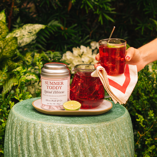 Summer Toddy with a glass of red brewed toddy on a green stool outdoors.