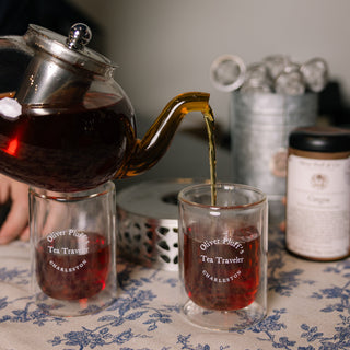 Tea being poured from a teapot into glass cups on a floral tablecloth.