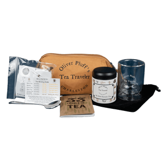 Tea travel set with a brown pouch, glass, jar, spoon, and notebook on a green background.