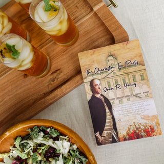 the charleston tea party book resting on table next to a bowl of salad and tray of iced teas