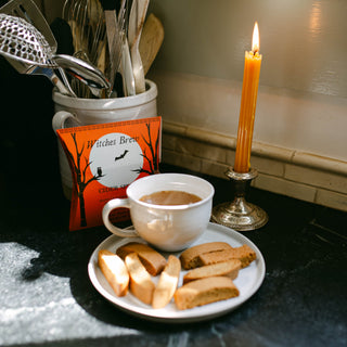 brewed cup of cider wassail in front of package of witches brew with lit candle