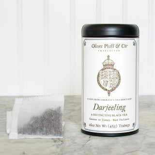 black tea tin with old timey crown graphic and white mesh tea bag sitting on white counter
