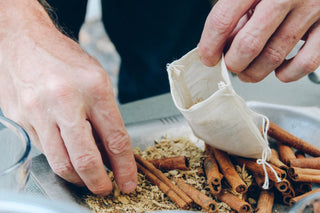 two man hands putting cinnamon sticks and loose leaf tea in white mesh tea bag