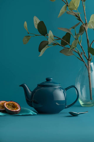 scenic photo of blue tea pot, figs, and a green plant with blue background