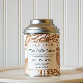 3oz West Indies Citrus loose tea tin complete with a large wire mesh tea brewing ball sitting on white plate