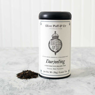 black tea tin with old timey crown graphic and a small pile of loose leaf tea beside. On white kitchen counter