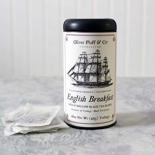 old timey ship graphic on black tea tin label, with white mesh tea bags beside it. on white kitchen counter