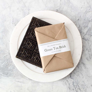 dark colored tea brick beside brown packaged brick sitting on white plate