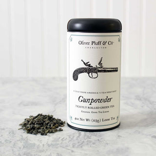 single black tea tin with old timey gun graphic on label beside a pile of loose leaf tea, sitting on white kitchen counter