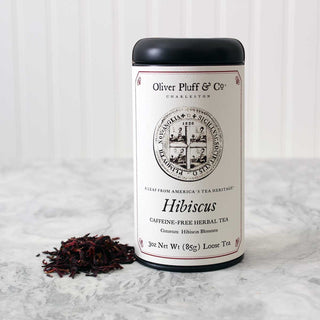 black tea tin against beside pile of dark loose leaf tea on white kitchen counter