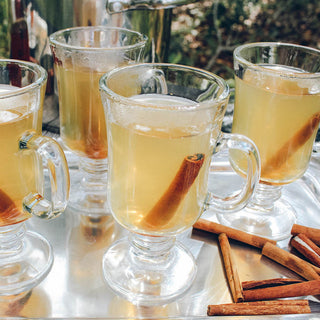 4 drinking glasses filled with refreshing tea and cinnamon sticks sitting on silver platter outside
