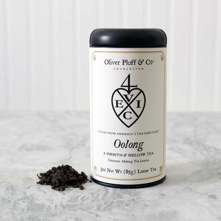 black tea tin with heart graphic on logo beside small pile of loose leaf tea sitting on white counter