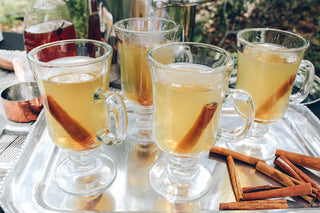 4 glass jars of tea and cinnamon sticks sitting on silver platter outside